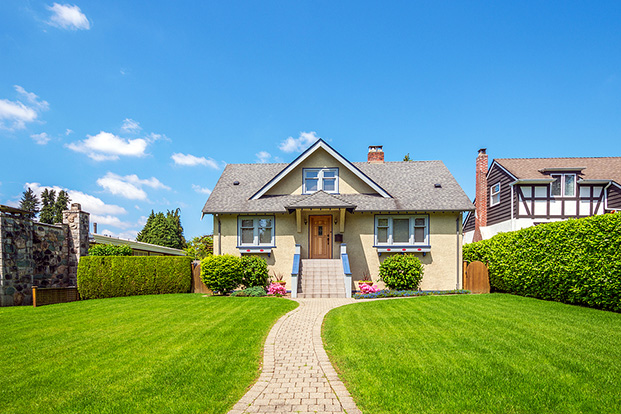 A cozy house with a neatly trimmed green lawn, a curved walkway leading to the front door, and a clear blue sky overhead.
